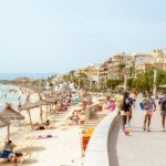 Spanish coastline with beach and pathway, with lots of people enjoy warm and sunny weather. Buying Rental Property for Long-term in ibiza